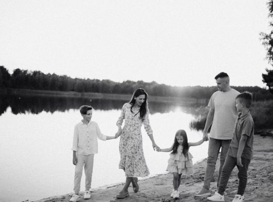 Monochrome photo of a family walking hand in hand along a serene lakeshore.