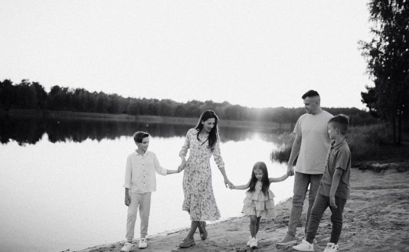 Monochrome photo of a family walking hand in hand along a serene lakeshore.